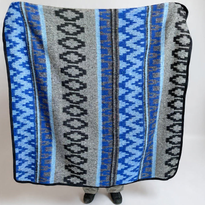 Blue and gray patterned blanket draped over a person on a white background