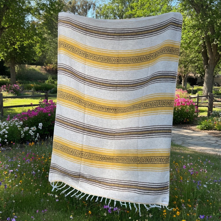 Striped towel on grass with flowers and trees in the background