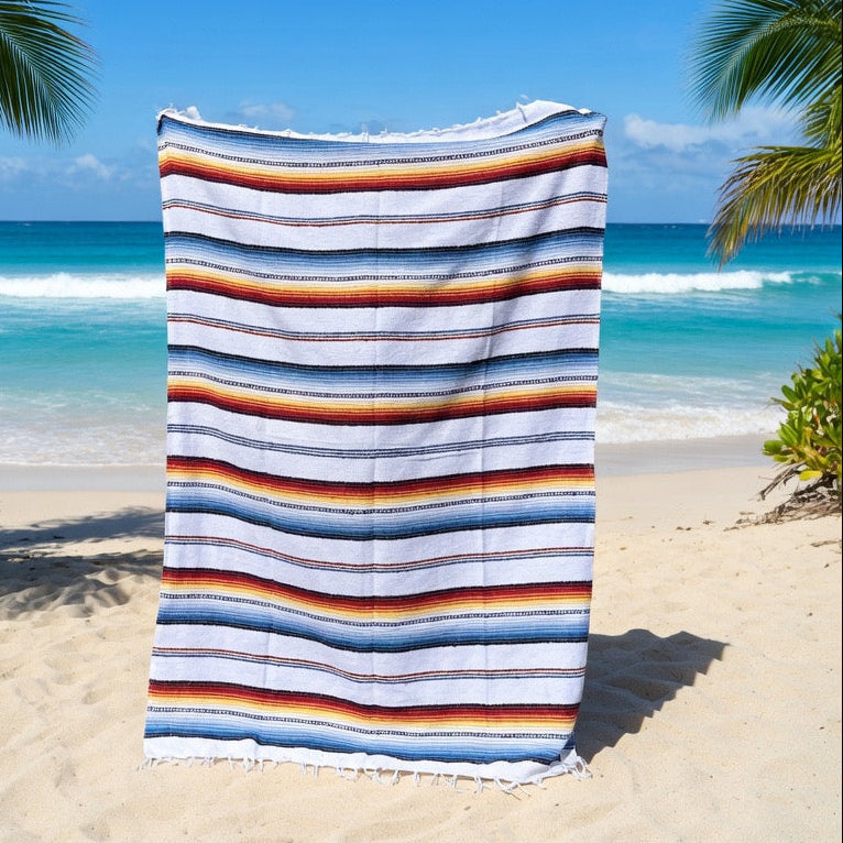 Striped beach towel on a sandy beach with ocean and palm trees in the background