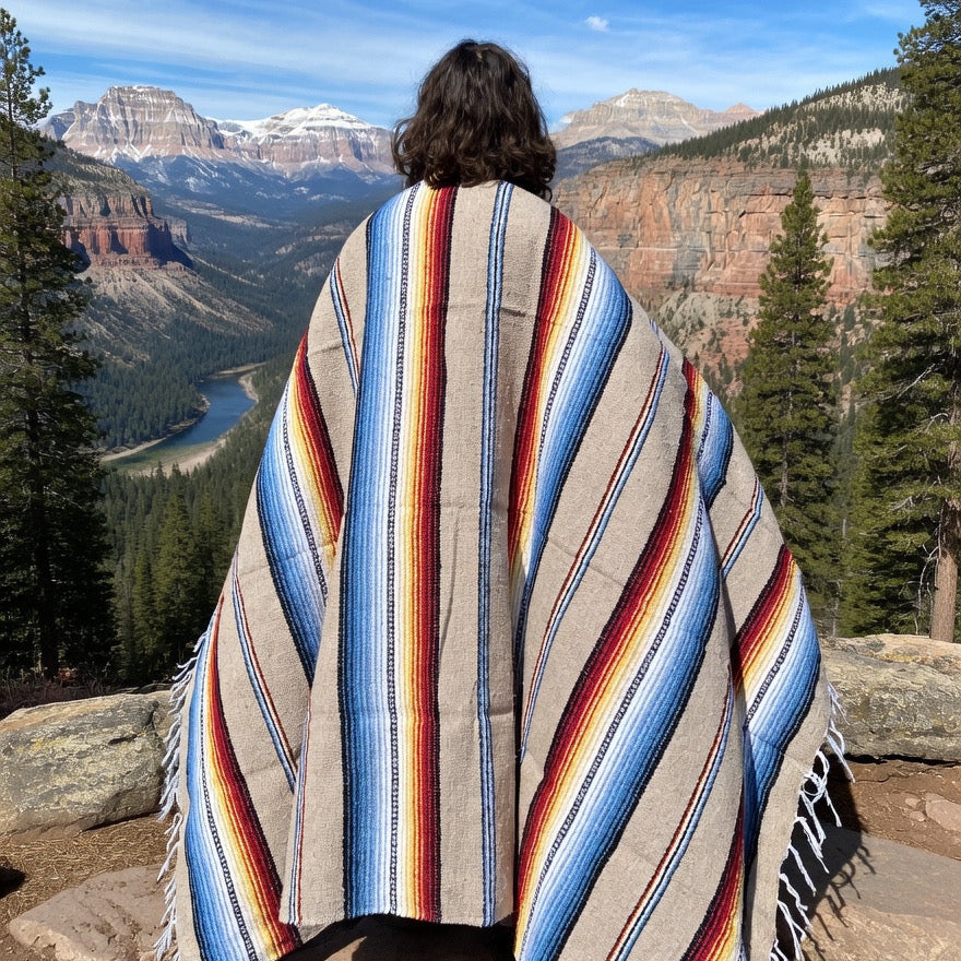 Person wrapped in a colorful striped blanket with a mountainous landscape in the background