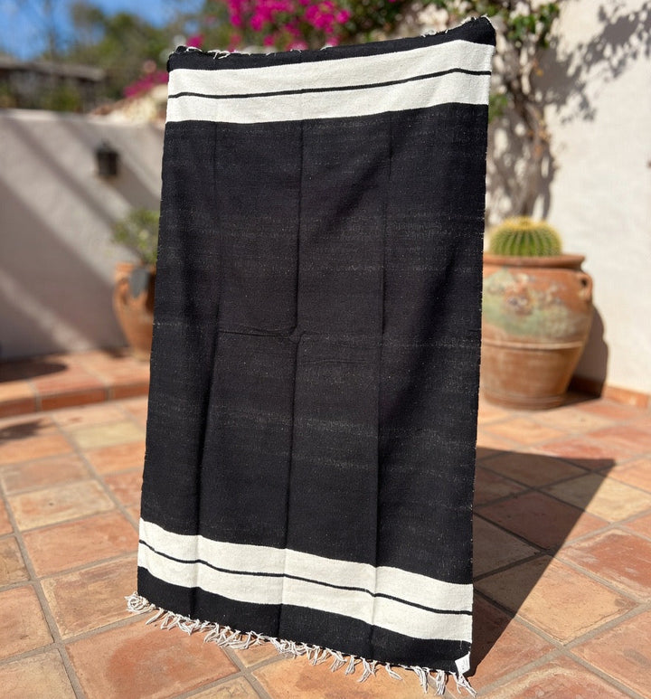 Black towel with white stripes on a tiled patio with plants in the background
