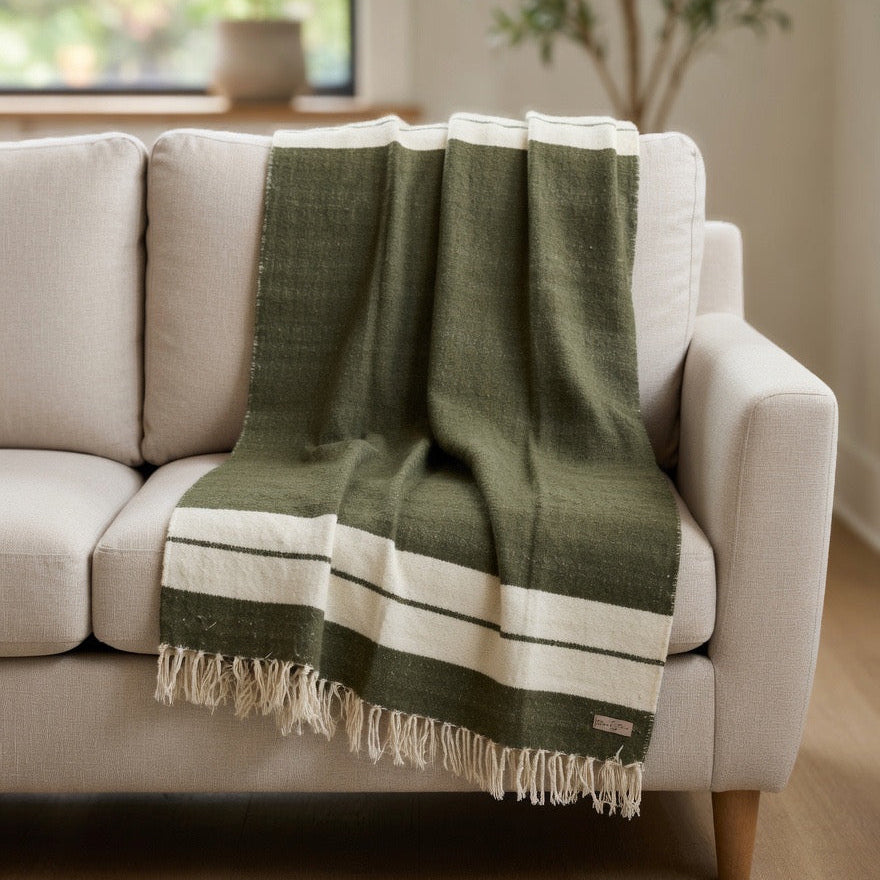 Green and white striped blanket draped over a beige sofa in a living room.