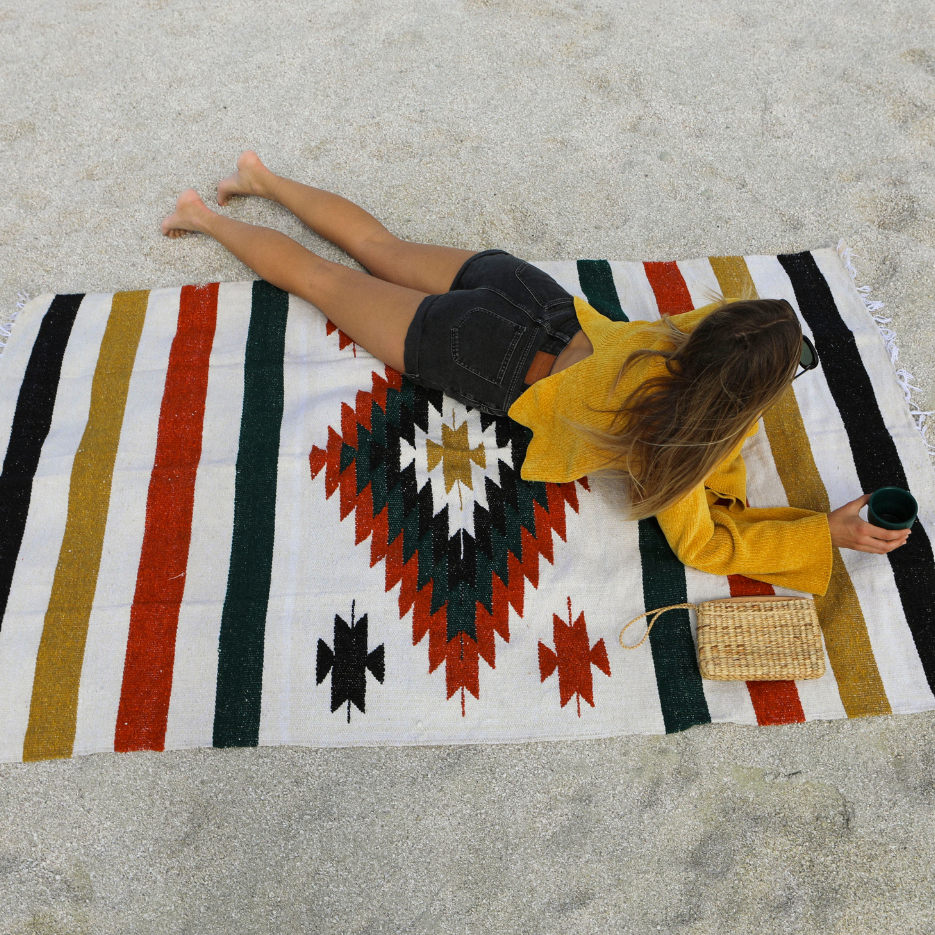 Person lying on a colorful patterned towel on a sandy surface