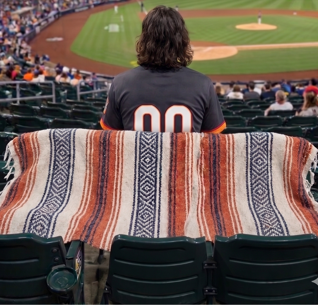Person sitting in a baseball stadium with a blanket, facing the field at night.