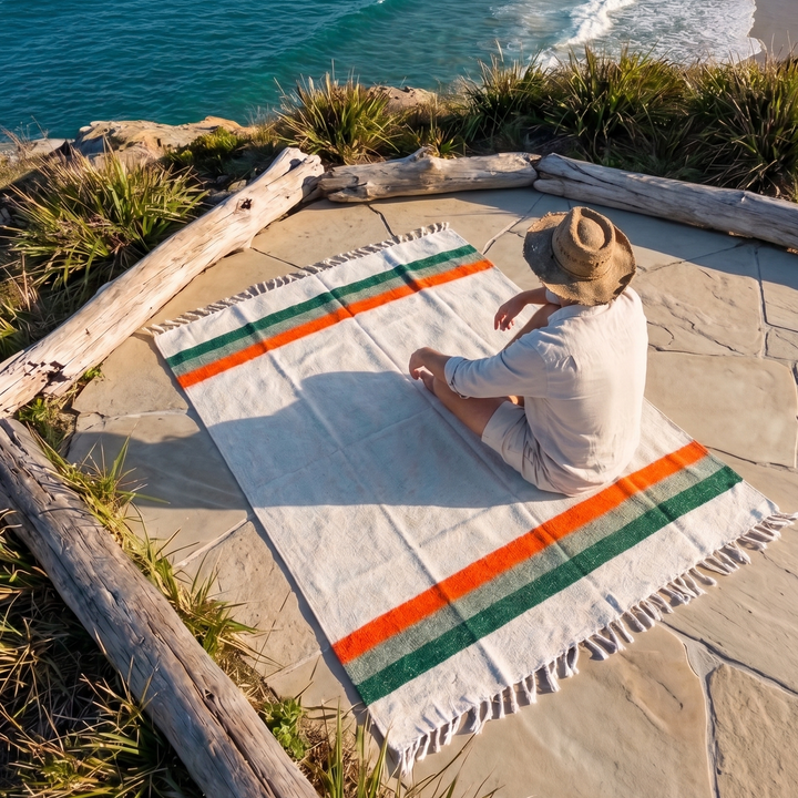 Person sitting on a striped blanket at a beach with ocean view