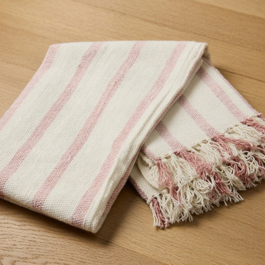 Pink and white striped blanket with fringes on a wooden floor