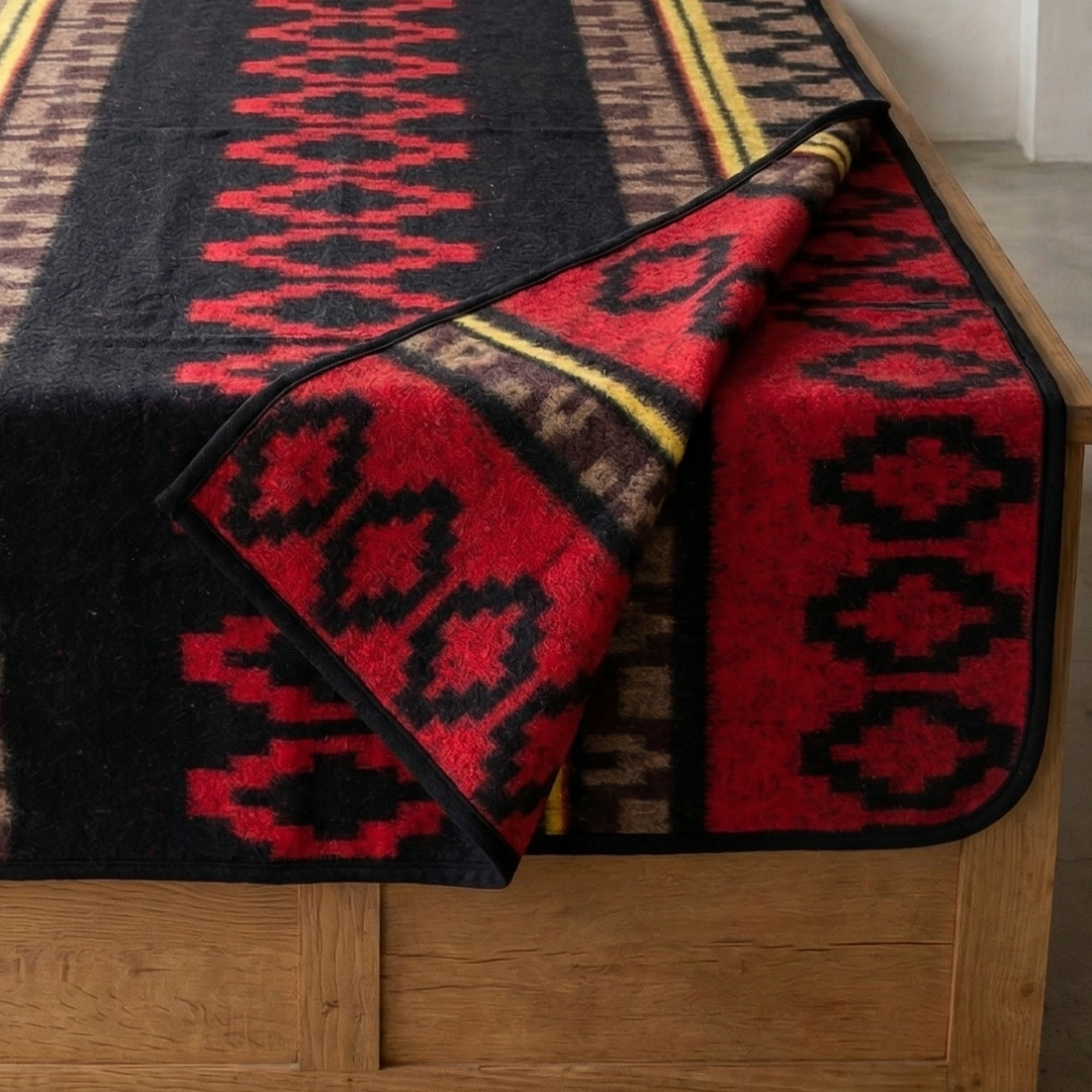 Woven blanket with geometric pattern draped over a wooden bench by a window.