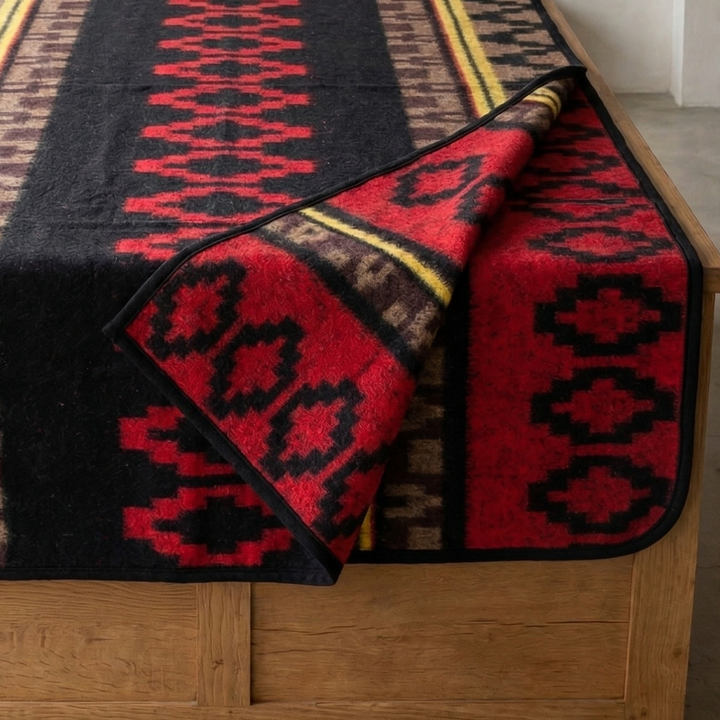Woven blanket with geometric pattern draped over a wooden bench by a window.