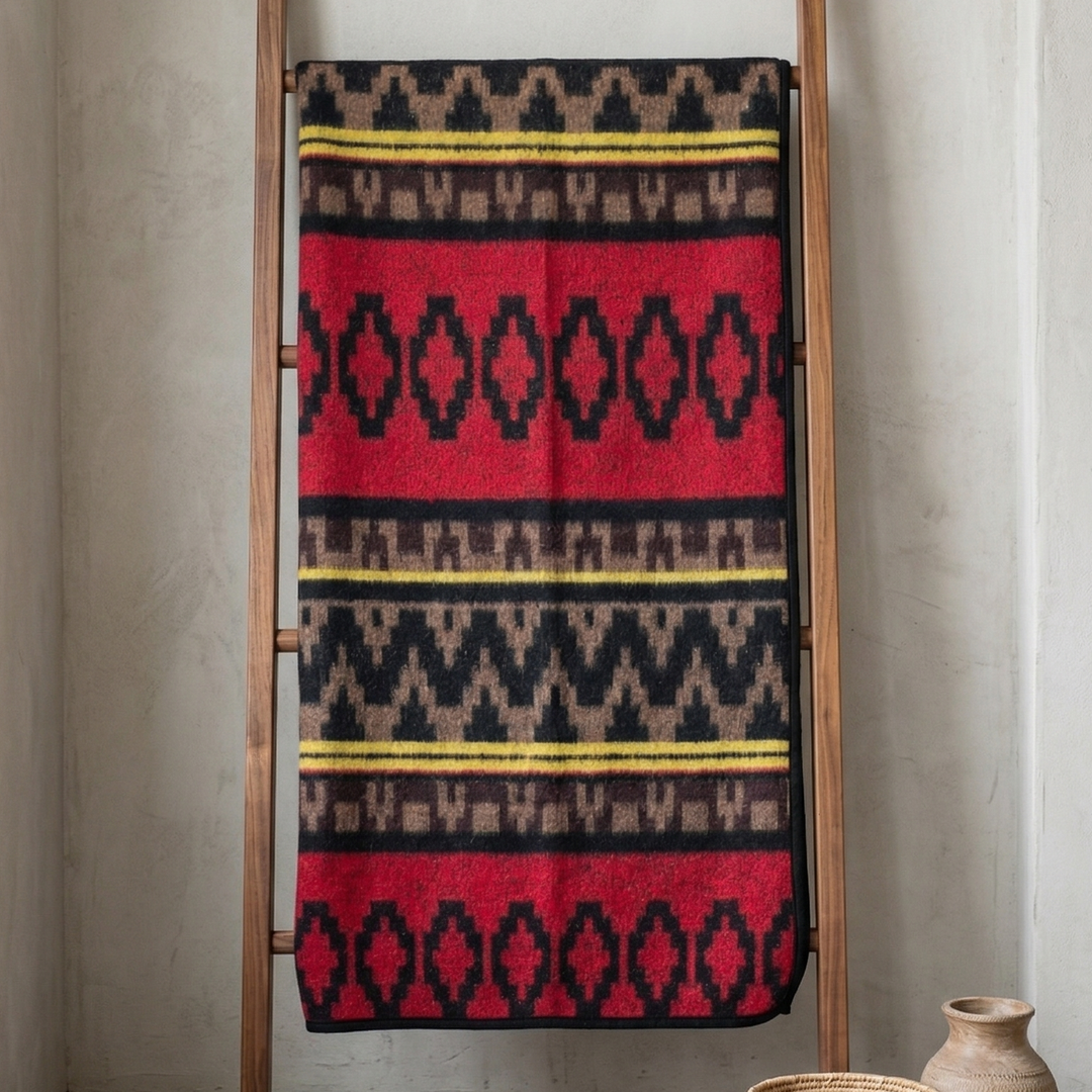 Patterned blanket on a wooden ladder against a neutral wall with decor items below.