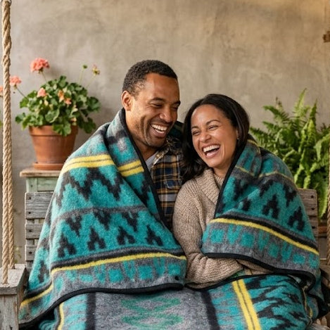 Couple wrapped in a patterned blanket on a porch with plants and flowers around.