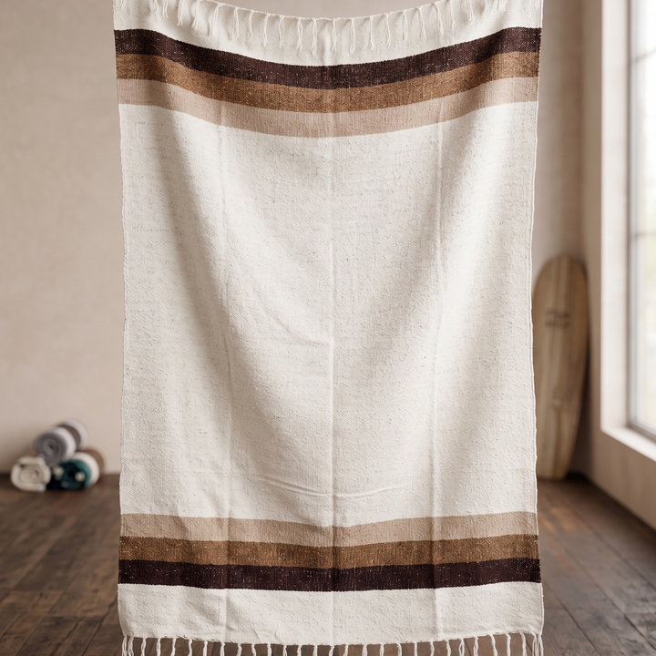 White blanket with brown stripes hanging on a rack in a bathroom.