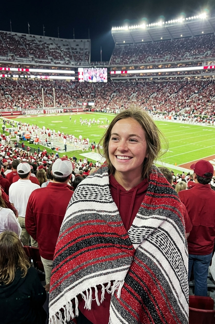 Fan wrapped in a Mexican stadium blanket in University of Alabama colors at a college football game