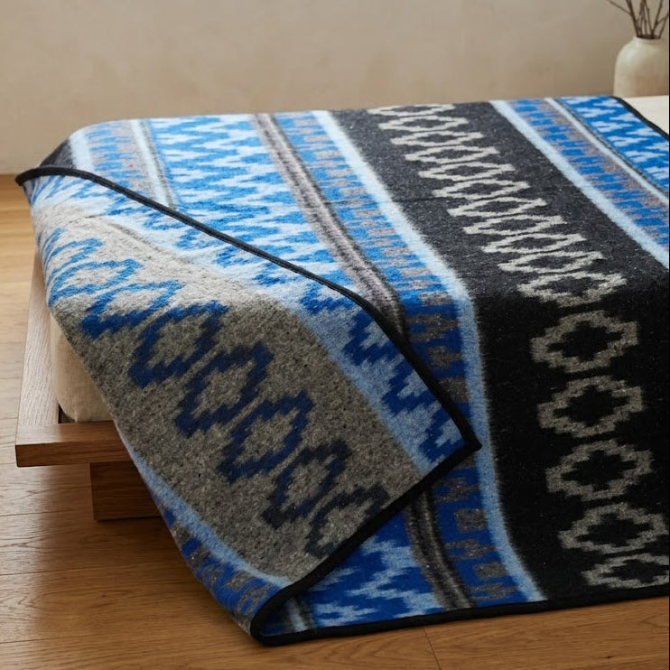 Patterned blanket draped over a bed in a room with wooden flooring.