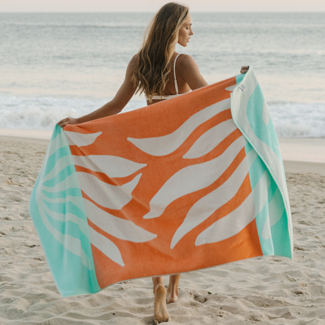 Woman holding a colorful beach towel on a sandy beach with ocean in the background