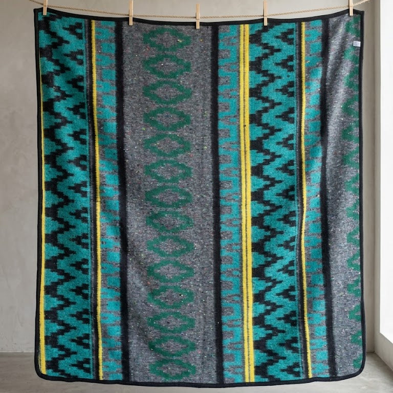 Patterned blanket with geometric design hanging on a line against a neutral wall.