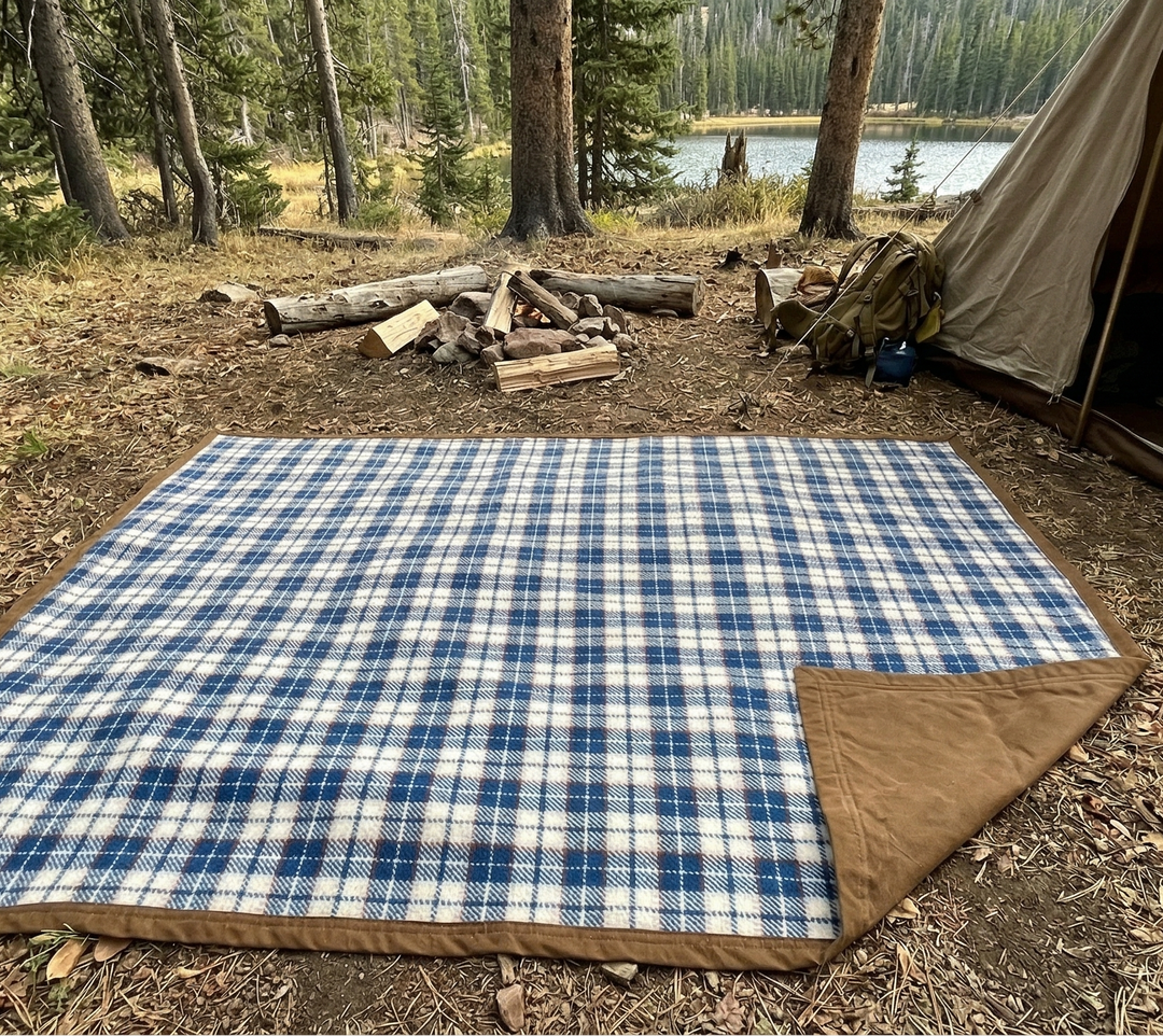Blue and white checkered blanket on the ground next to a tent in a forest setting.
