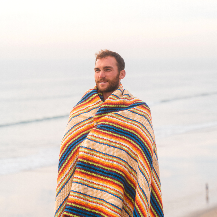 Rainbow Povoa blanket wrapped around model at the beach